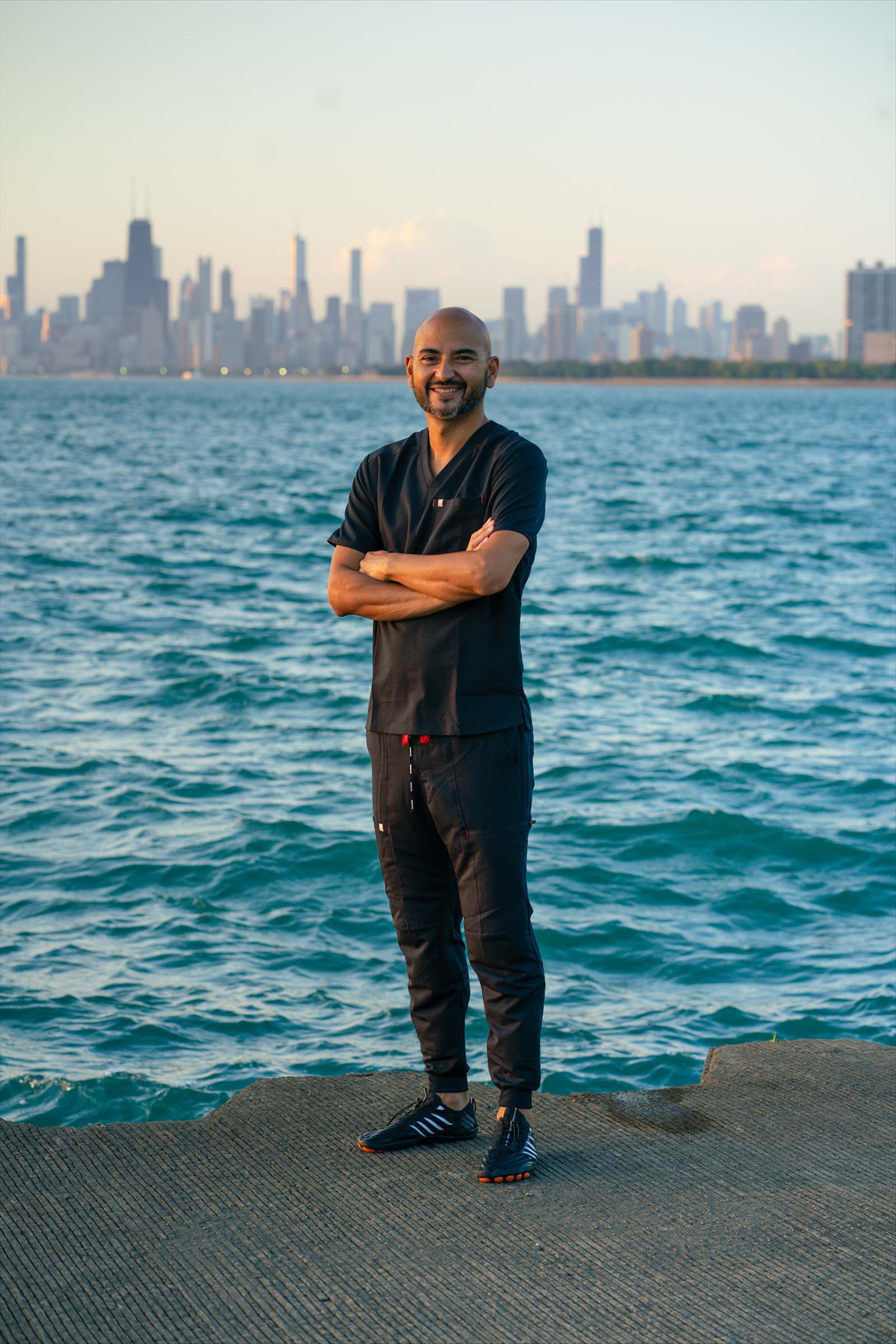 Rios, a smiling massage therapist in scrubs, standing along the Chicago lakefront with the skyline in the background